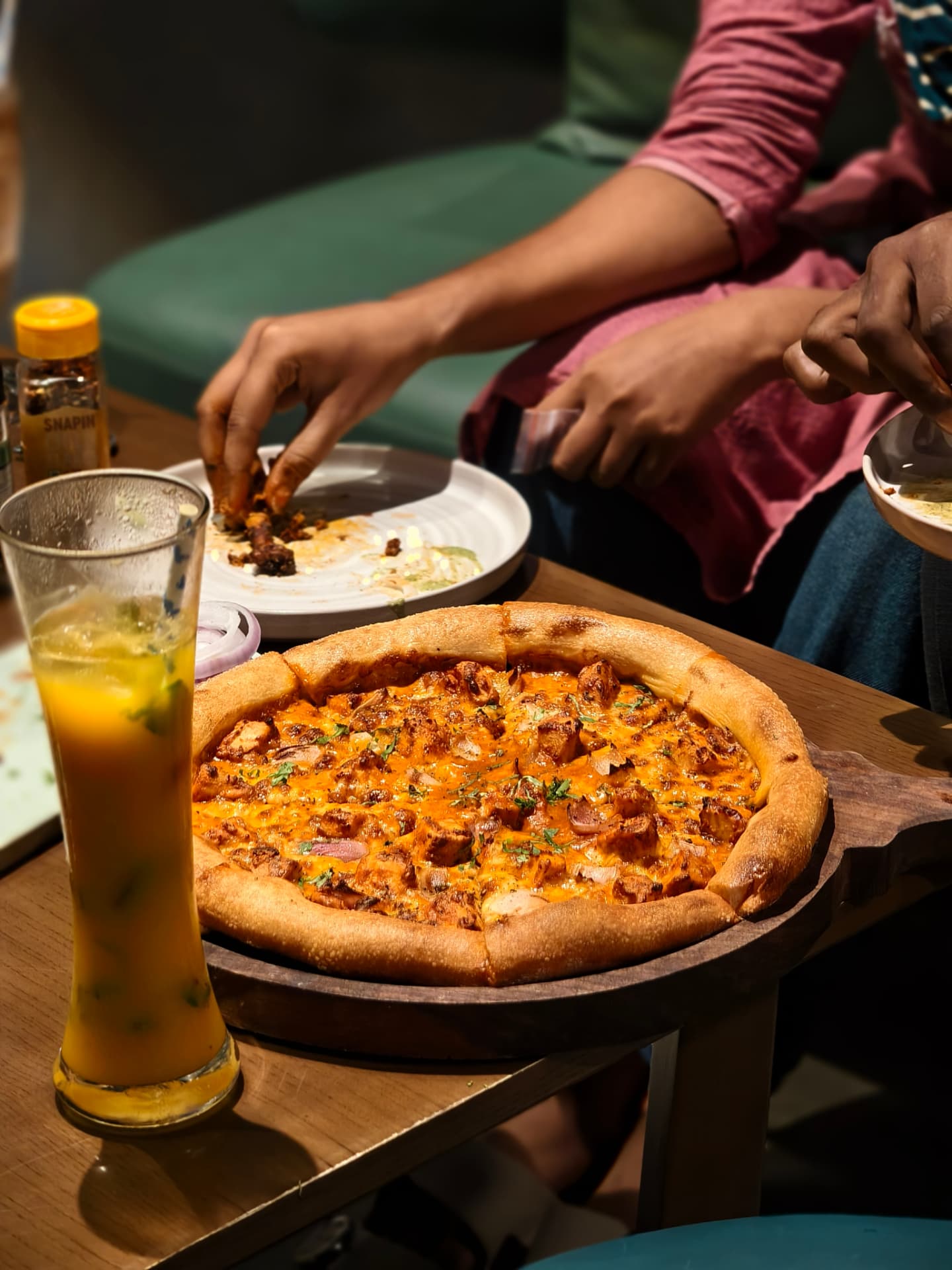 Pizza on a wooden board with a cold drink at an O’Co table